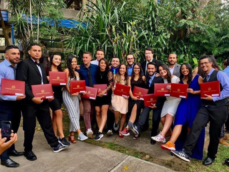 Imagen de grupo de estudiantes con zapatos deportivos, sosteniendo sus títulos de graduación al aire libre