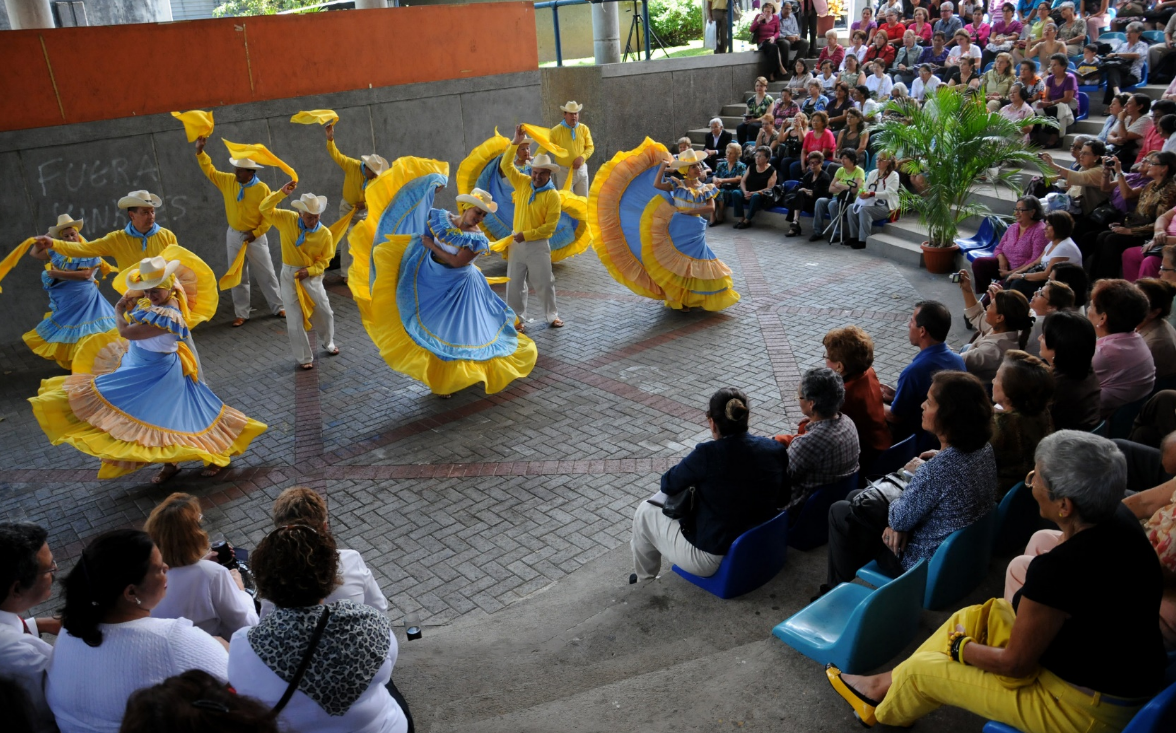 Grupo de adultos con trajes típicos celeste y amarillo bailando