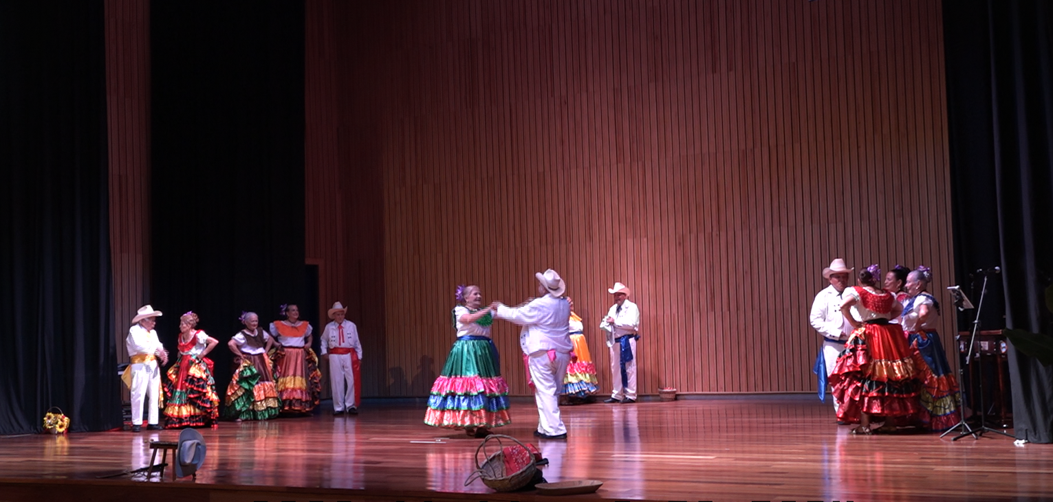 Imagen de adultos mayores bailando con trajes típicos en escenario